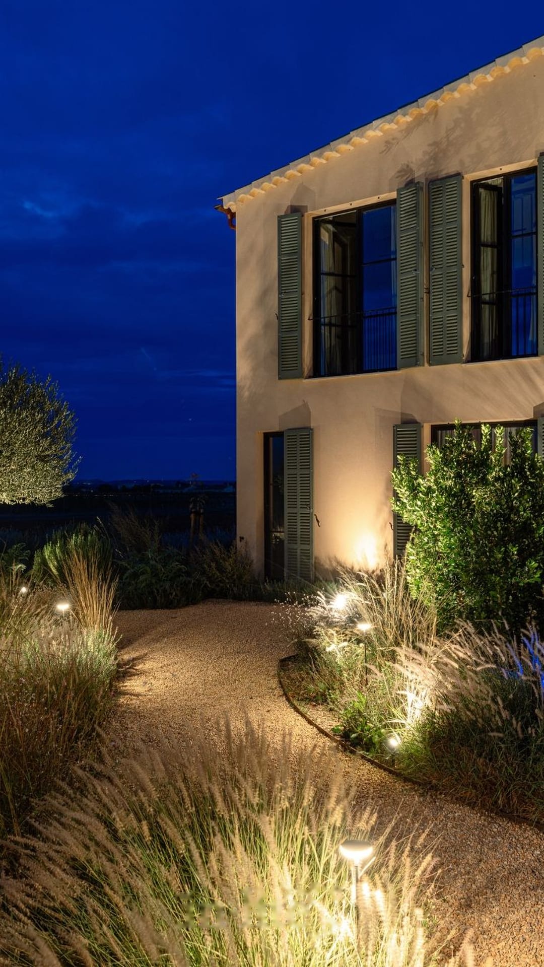 Villa de piedra con persianas y balizas entre gramíneas ornamentales