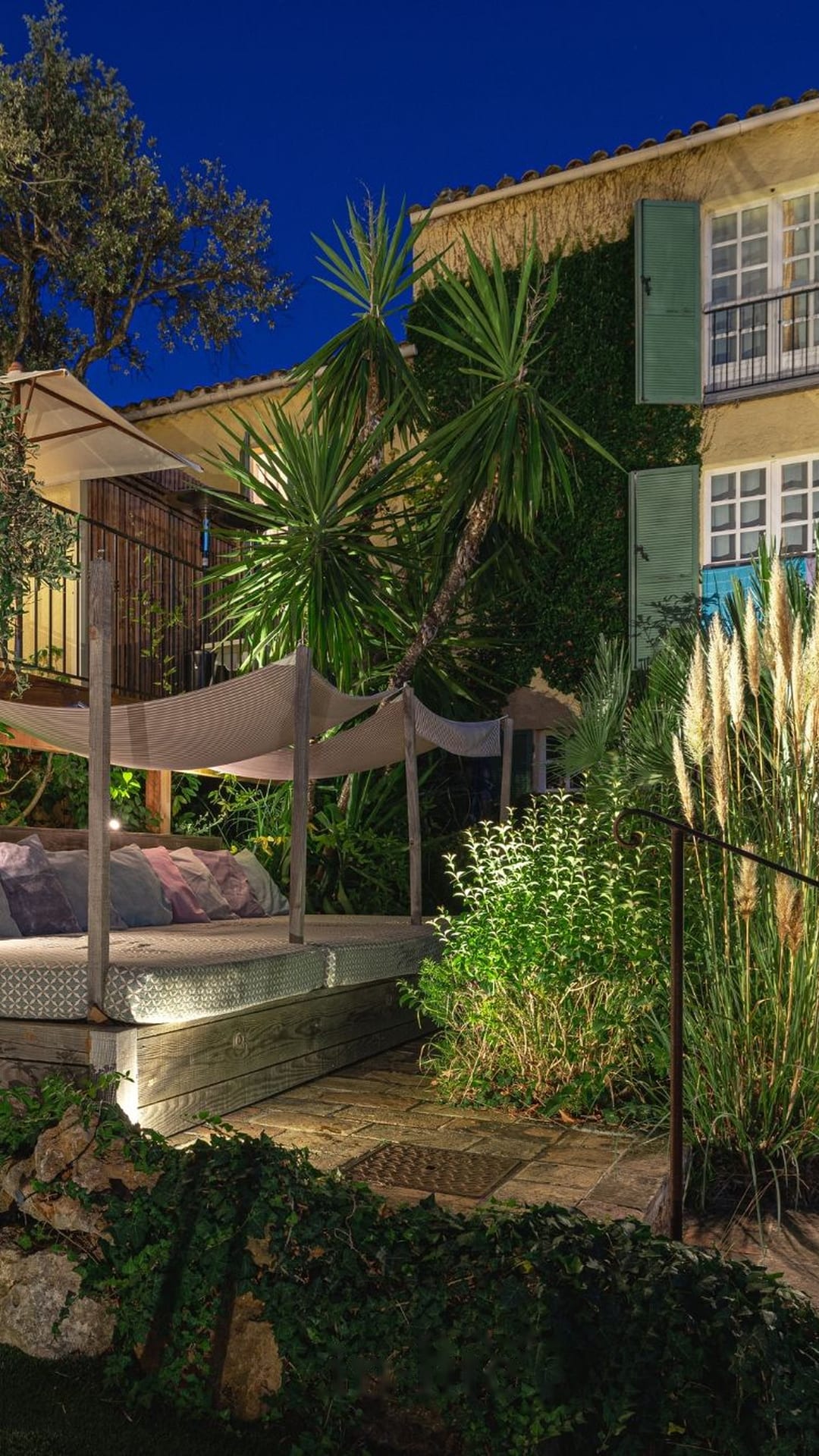 Patio con terraza, palmera y toldo vela iluminados al atardecer