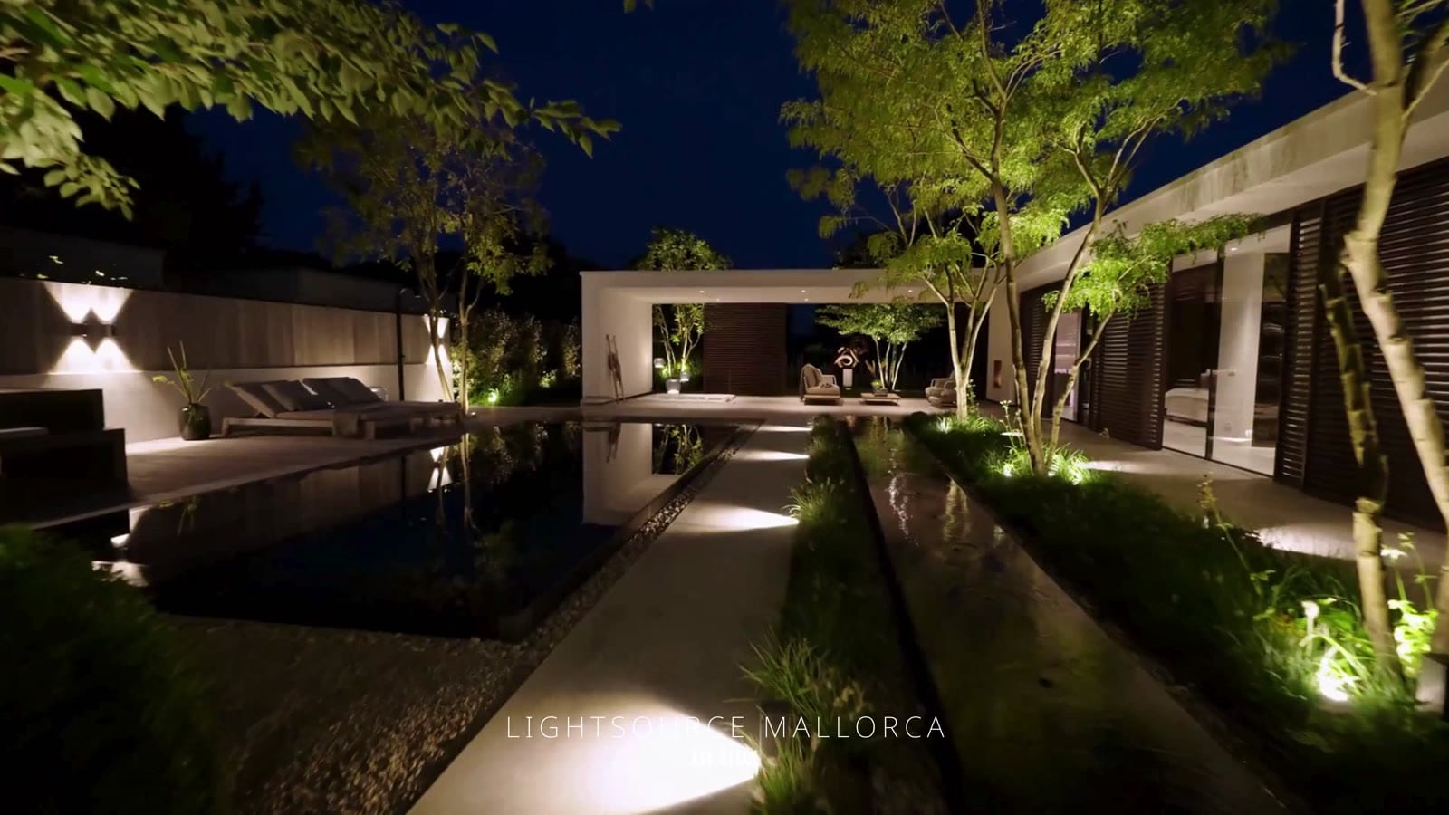 Villa contemporánea de noche con árboles iluminados, láminas de agua y empotrables de suelo en Mallorca